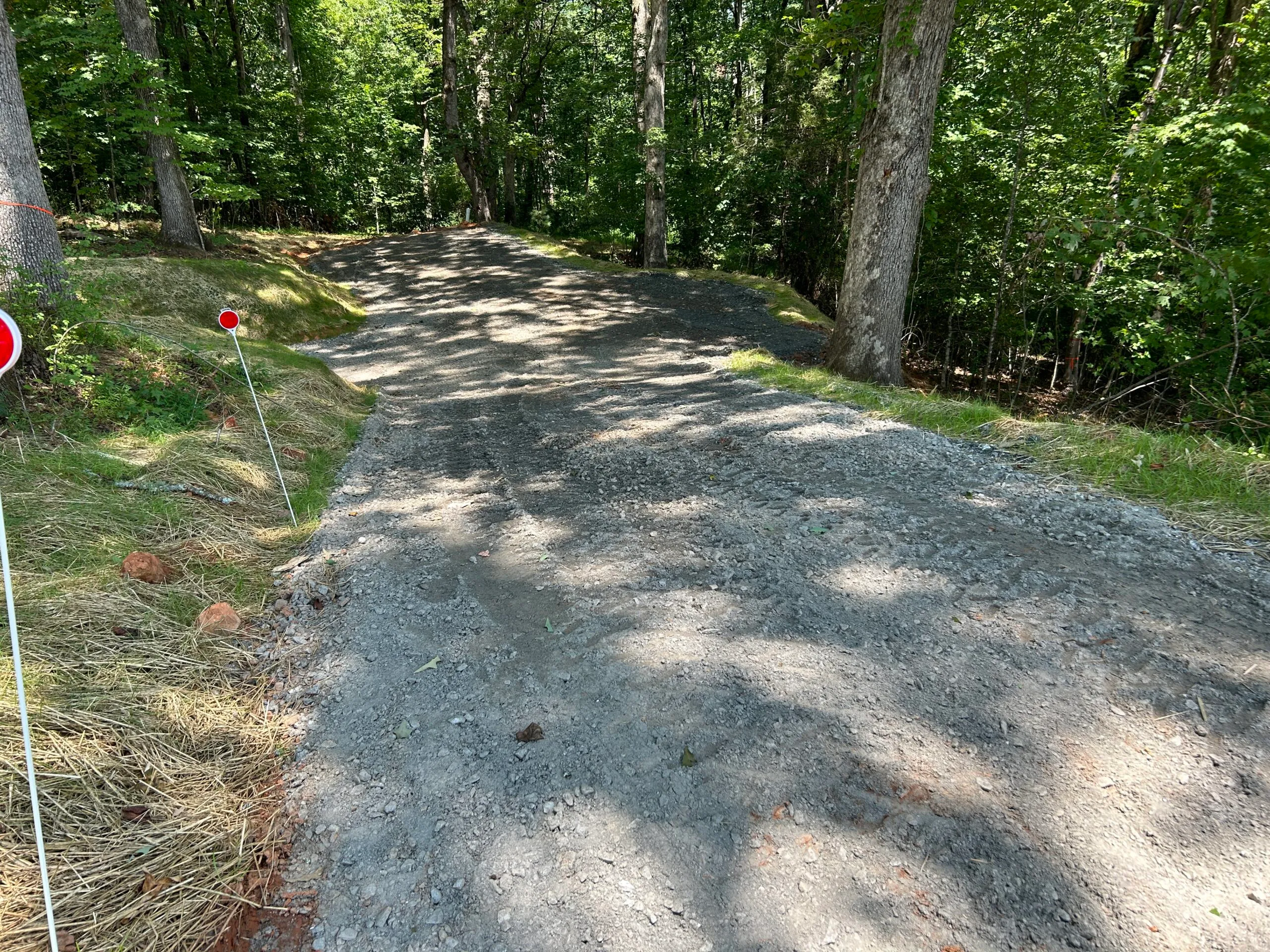 Gravel road winding through a wooded area, marked by red signs on white posts.