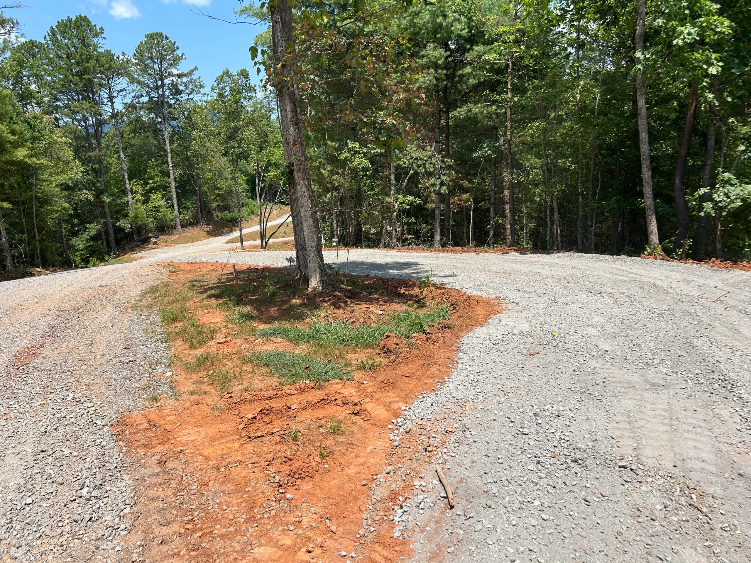 A gravel road curves through a wooded area, leading to a fork where one path continues straight and the other turns right.