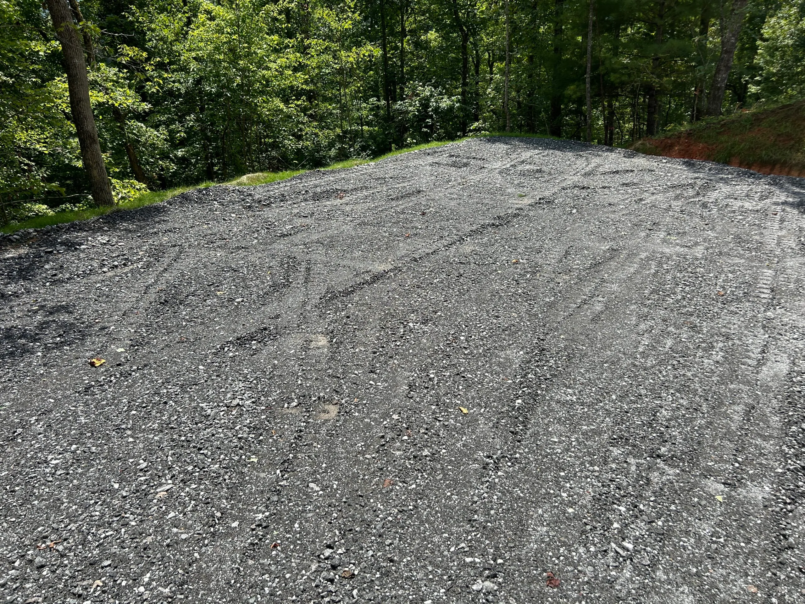 Gravel surface cleared in a wooded area, featuring tire tracks.