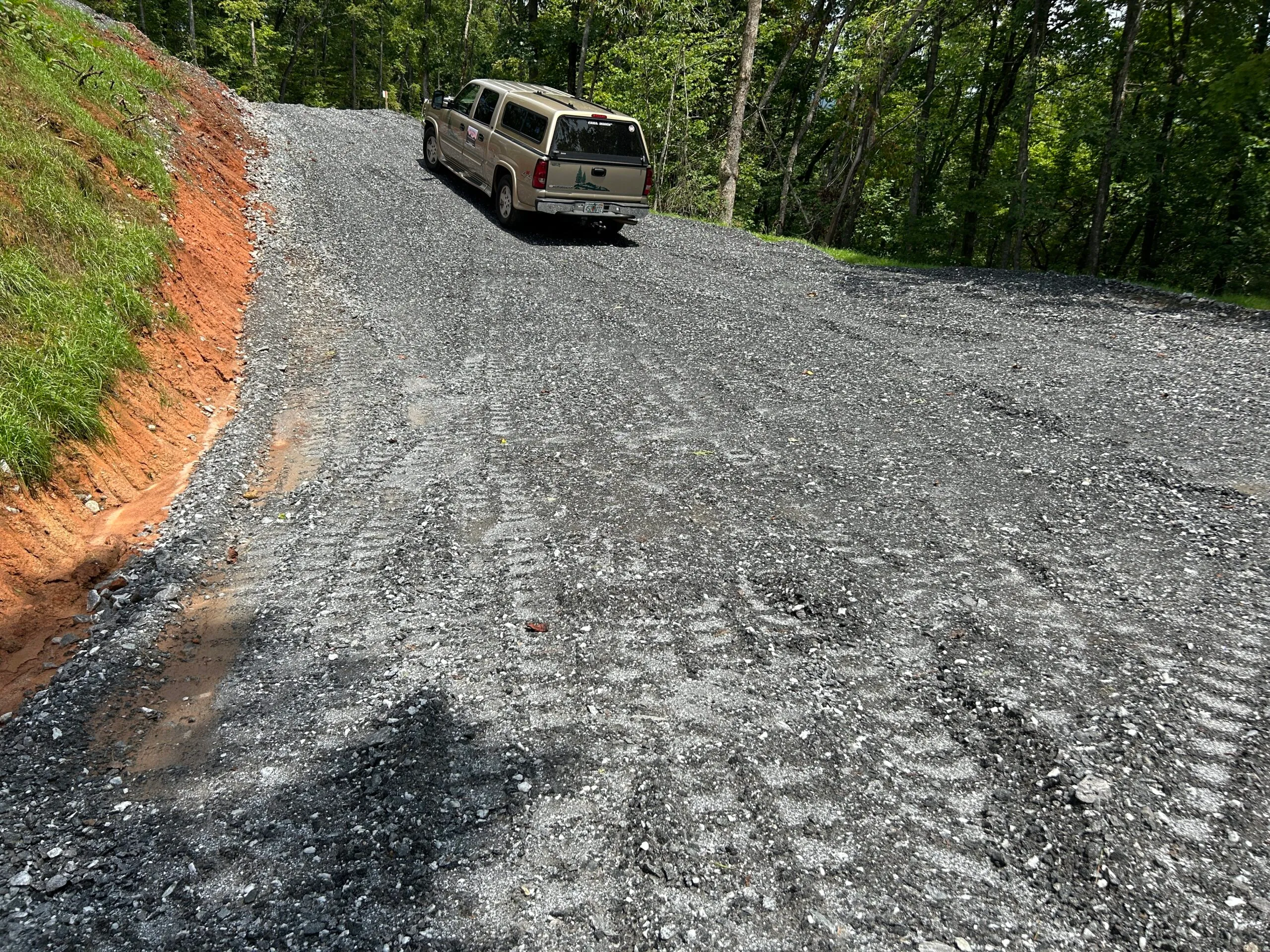 A gravel driveway winds up a hillside, with a beige truck parked on the path